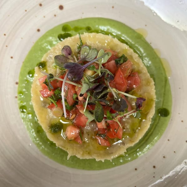 Mediterranean dish with green sauce, a yellow base, diced tomatoes, and microgreens on a white plate.