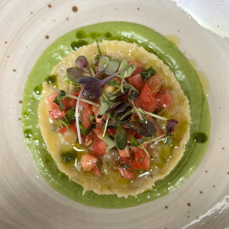 Mediterranean dish with green sauce, a yellow base, diced tomatoes, and microgreens on a white plate.