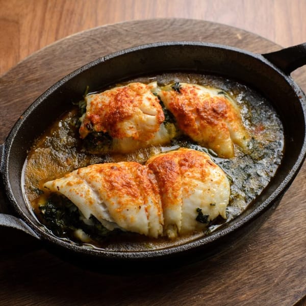 Three Mediterranean fish fillets with red spice and dark greens in a cast iron pan.
