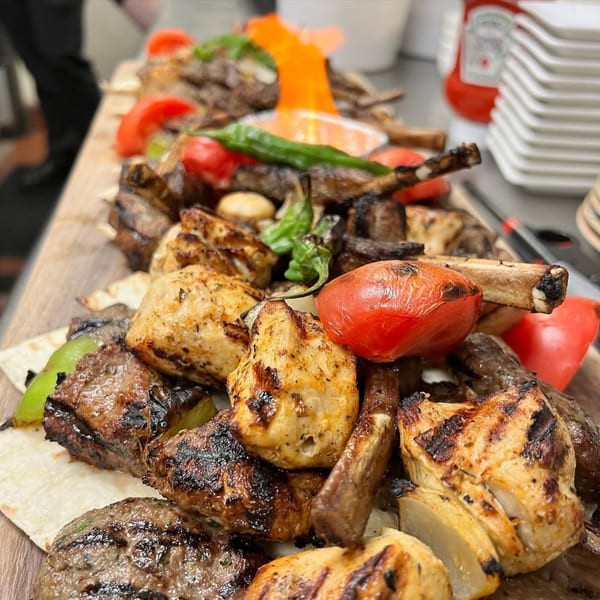 A large platter of grilled Mediterranean meats, vegetables, and flatbread on a wooden board.