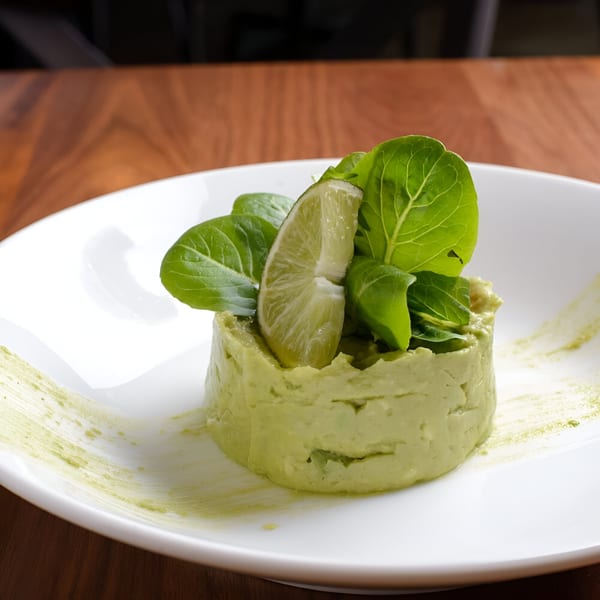 A molded avocado dish topped with fresh greens and a lime wedge on a white plate.
