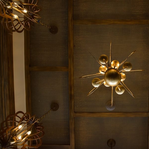 Ornate golden chandeliers hang from a dark, textured ceiling with wooden beams at Krinti Mediterranean Grill.