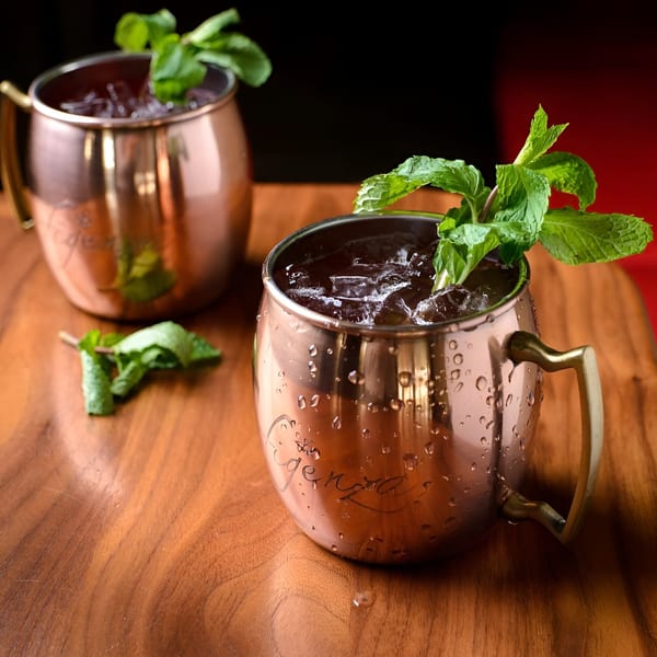 Two copper mugs filled with iced drinks and garnished with fresh mint sprigs on a wooden table.