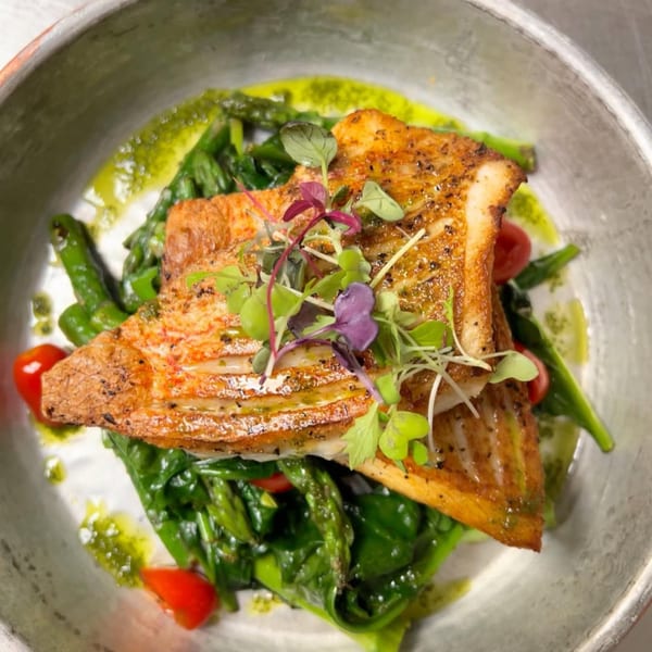 Pan-seared fish with crispy skin, served over green vegetables, cherry tomatoes, and microgreens.