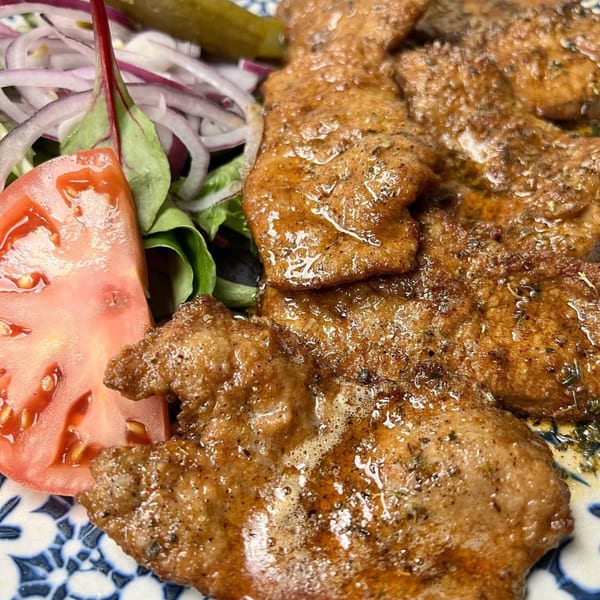 Close-up of grilled Mediterranean meat with a side of fresh salad, tomato, and red onions.