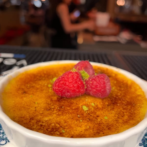 Close-up of a crème brûlée with raspberries and lime zest, in a white ramekin.